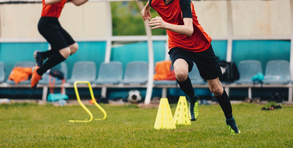Boy Soccer Player In Training. Boys Running Between Cones and Jumping During Practice in Field on Sunny Day. Young Soccer Players at Speed and Agility Practice Session