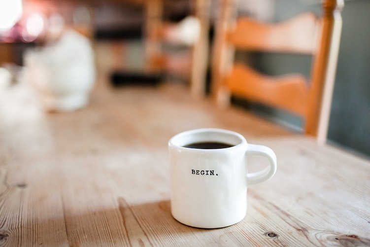 A white ceramic mug on the table with the text “begin” written on it