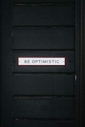 “be optimistic” written on a wooden door