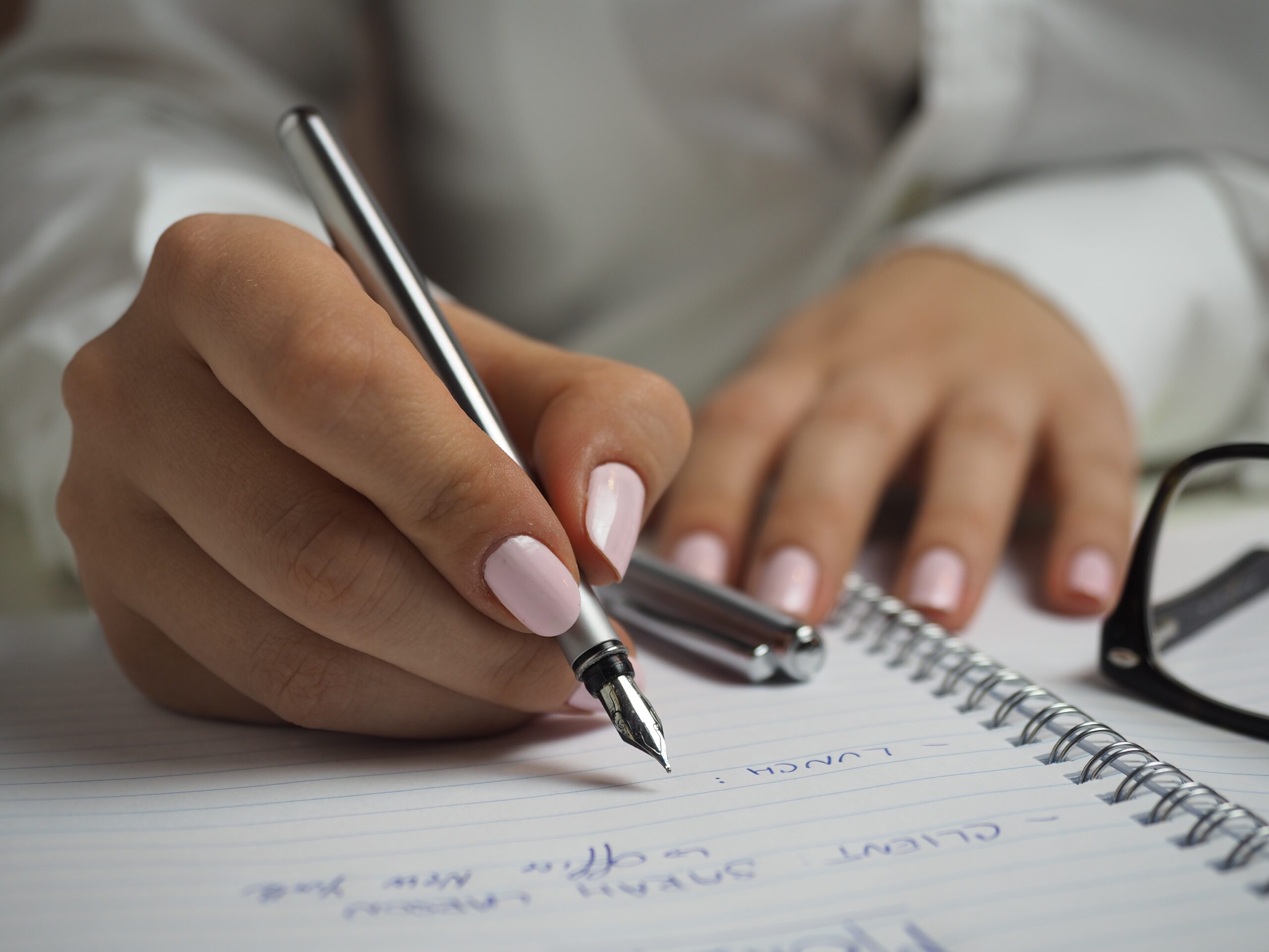 woman-in-white-long-sleeved-shirt-holding-a-pen-writing-on-a-paper