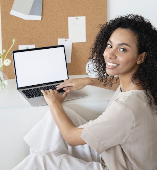 A-woman-smiling-at-the-camera-while-using-her-laptop